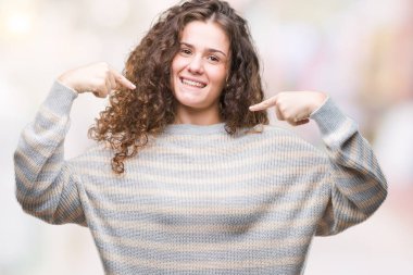 Yüzünde gülümseme ile kendinden emin görünüyorsun, kendini gururlu ve mutlu parmakları ile işaret izole arka plan üzerinde kış kazak giyen güzel esmer kıvırcık saçlı Genç kız.