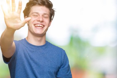 Yakışıklı delikanlı gösterilen ve parmakları ile işaret izole arka plan üzerinde mavi t-shirt giyen beş kendinden emin ve mutlu gülümseyerek iken numara.