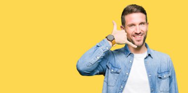 Yakışıklı adam mavi gözleri ve denim ceket gülümseyen giyen sakal el ve parmak telefonda konuşmak ile telefon jest yapıyor. Kavramları iletişim.
