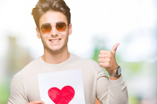 Joven Hombre Guapo Sosteniendo Tarjeta Con Corazón Rojo Sobre Fondo — Foto de Stock