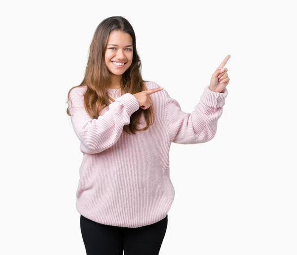 年轻美丽的黑发女人穿着粉红色的冬季毛衣在孤立的背景微笑着 看着相机指向用两只手和手指的一侧 — 图库照片