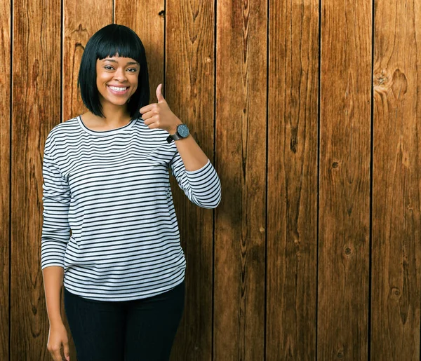 Hareketi el ile mutlu yaşasın yapıyor izole arka plan üzerinde çizgili süveter giyen güzel genç Afro-Amerikan kadın. Başarı gösteren kameraya bakarak ifade onaylama.