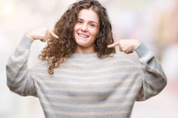 Yüzünde gülümseme ile kendinden emin görünüyorsun, kendini gururlu ve mutlu parmakları ile işaret izole arka plan üzerinde kış kazak giyen güzel esmer kıvırcık saçlı Genç kız.
