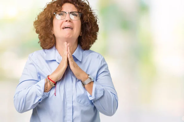 Beautiful middle ager senior businees woman wearing glasses over isolated background begging and praying with hands together with hope expression on face very emotional and worried. Asking for forgiveness. Religion concept.