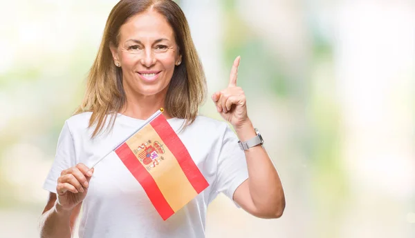 中年西班牙妇女拿着西班牙国旗在孤立的背景惊讶的想法或问题用幸福的脸指指点点 — 图库照片