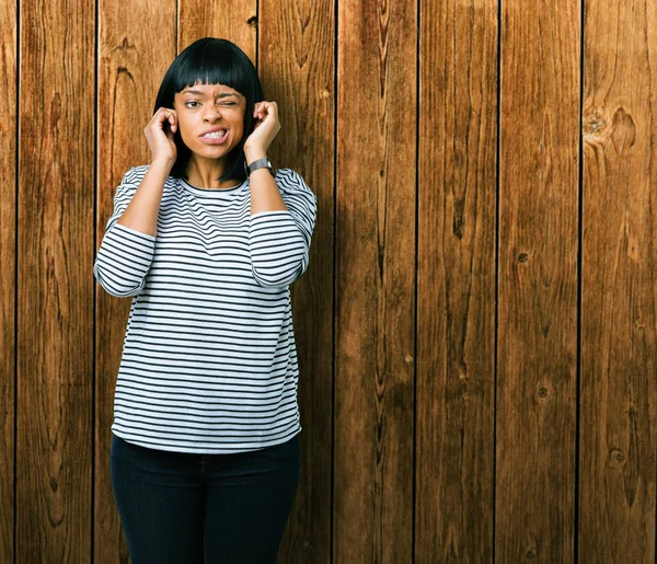 Yüksek sesle müzik gürültü rahatsız ifade parmaklarıyla kulaklarıyla kapsayan izole arka plan üzerinde çizgili Süveter giyen güzel genç Afro-Amerikan kadın. Sağır kavramı.