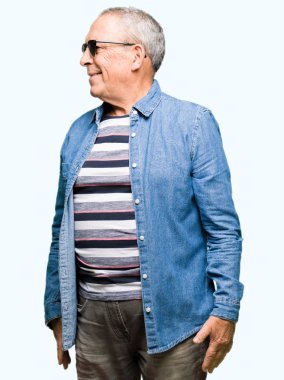 Yakışıklı kıdemli dostum giyen denim ceket ve uzak yan yüzünde, doğal ifade gülümseme ile seyir güneş gözlüğü. Kendine güvenen gülüyor.