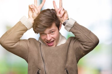 Neşeli gülümseyen izole arka plan tavşan kulakları, komik ve çılgın baş parmaklar ile poz üzerinde kış ceket giyen genç yakışıklı adam