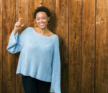 İzole arka plan gülümseyen ve süre seyir ve kamera boyutu işaret parmaklarıyla yapıyor el ile kendinden emin eller üzerinde bir kazak giyen genç güzel Afrikalı-Amerikalı kadın. Ölçü kavramı.