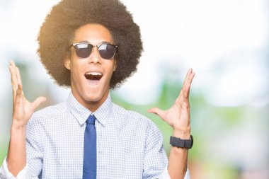 Genç Afro-Amerikalı iş adamı afro saçlı deli ve çığlık kaldırdı ve açık gözleri heyecanlı silah ile başarı için hayran kutluyor güneş gözlüğü takıyor. Kazanan kavramı