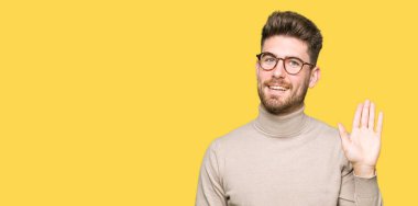 Giyen genç yakışıklı iş adamı mutlu Selam Waiving gözlük ve gülümseyen, dostça jest hoş geldiniz