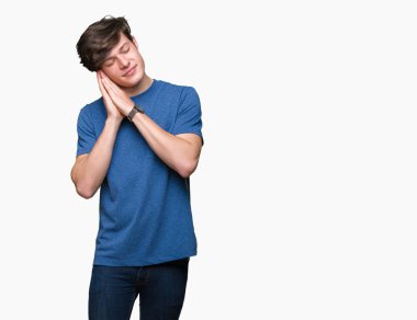 Uyku yorgun hayal ve ellerle birlikte poz ile kapalı gözler gülümseyen izole arka plan üzerinde mavi t-shirt giyen genç yakışıklı adam.