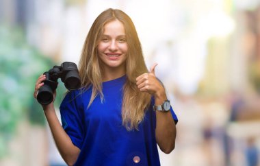 Dürbün ile ok işareti, başparmak ile parmak, mükemmel işareti yapıyor kocaman bir gülümseme ile izole arka plan üzerinde mutlu arayan genç güzel sarışın kadın