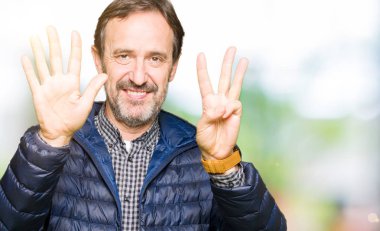 Kış ceket gösterme ve parmakları ile işaret giyen orta yaş yakışıklı adam kendinden emin ve mutlu gülümseyerek süre sekiz numara.