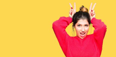 Neşeli gülümseyen kırmızı kazak ve komik ve çılgın baş parmaklar ile kulakları, tavşan poz topuz giyen genç güzel kadın