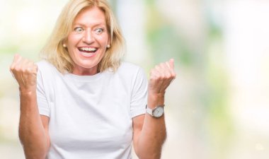 Orta yaş sarışın kadın kutluyor izole arka plan üzerinde şaşırttı ve başarı için kaldırdı kollarını açarak hayret ve gözleri açık. Kazanan kavramı.