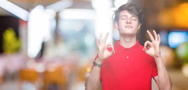 İzole arka plan üzerinde kırmızı t-shirt giyen genç yakışıklı adam rahatla ve gülümseyen gözlerle kapalı parmak jestle meditasyon yapıyor. Yoga kavramı.