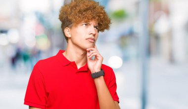 Çene düşünme hakkında soru, dalgın ifade üzerine el ile kırmızı t-shirt giyen afro saçlı Genç yakışıklı adam. Düşünceli yüzüyle gülümsüyor. Şüphe kavramı.