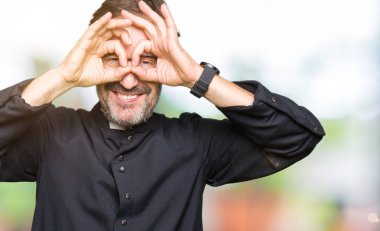 Katolik giyen orta yaş rahip adam robe dilini, parmaklarının arasından baktığını yapışmasını dürbün gibi ok jest yapıyor. Deli ifade.