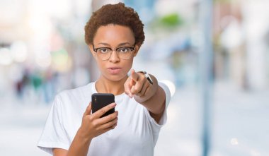 Kamera ve size parmak ile işaret arka plan üzerinde akıllı telefon kullanan genç Afro-Amerikan kadın izole, el işareti, pozitif ve kendinden emin bir jest ön