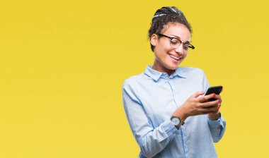 Genç izole arka plan üzerinde duran ve diş gösterilen kendine güvenen bir gülümsemeyle gülümseyerek mutlu bir yüz ile akıllı telefon kullanan saç Afro-Amerikan iş kız örgülü