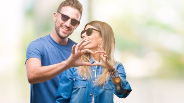 Genç çift aşık aşık kalp simgesi ve elleriyle şekil gösteren gülümseyen izole arka plan üzerinde güneş gözlüğü takıyor. Romantik kavramı.