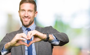 Takım elbise ve kravat aşık kalp simgesi ve elleriyle şekil gösteren gülümseyen giymiş yakışıklı iş adamı. Romantik kavramı.