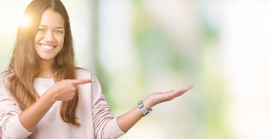 Hayret ve el ile sunulması ve parmak ile işaret ederken kameraya gülümseyen izole arka plan üzerinde pembe kazak giyen genç güzel esmer kadın.