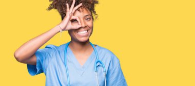 Genç Afro-Amerikan doktor kadın gülümsüyor, parmakları ile mutlu yüz üzerinden seyir göz el ile ok jest yapıyor izole arka plan.