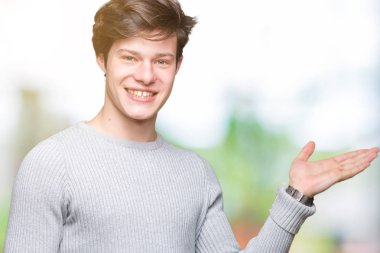 Neşeli sunulması ve kameraya bakarak avucunun ile işaret gülümseyen izole arka plan üzerinde kış kazak giyen genç yakışıklı adam.