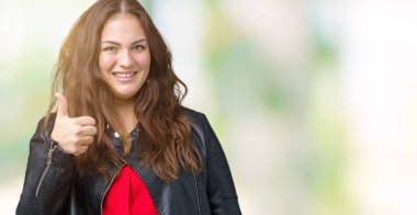 Artı boyutu genç kadın güzel üzerinde bir moda deri ceket giyiyor hareketi el ile mutlu yaşasın yapıyor arka plan izole. Başarı gösteren kameraya bakarak ifade onaylama.