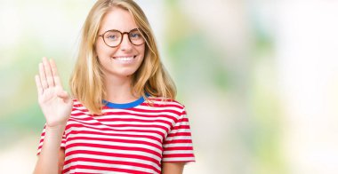 İzole arka plan Waiving mutlu selam söyleyerek üzerinde gözlük ve gülümseyen, dostça karşılama jest giyen güzel genç kadın