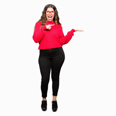 Hayret ve el ile sunulması ve parmak ile işaret ederken kameraya gülümseyen kırmızı gözlük takan genç güzel kadın.