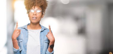 Güzel genç Afro-Amerikan kadın hayrete ve yukarıya bakıyor ve parmakları ile işaret ve silah kaldırdı sürpriz izole arka plan üzerinde gözlük.