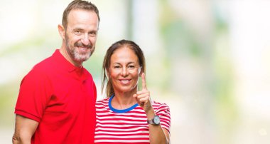 Orta yaş İspanyol çift ve parmak gülümseyen süre bir numara ile kendinden emin ve mutlu yukarıyı gösteren izole arka plan üzerinde aşık.