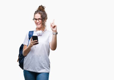 Sırt çantası, kulaklık ve smartphone izole arka plan üzerinde giyen genç esmer öğrenci kız bir fikir ya da soru işaret parmağı gülen yüz, bir numara ile şaşırttı