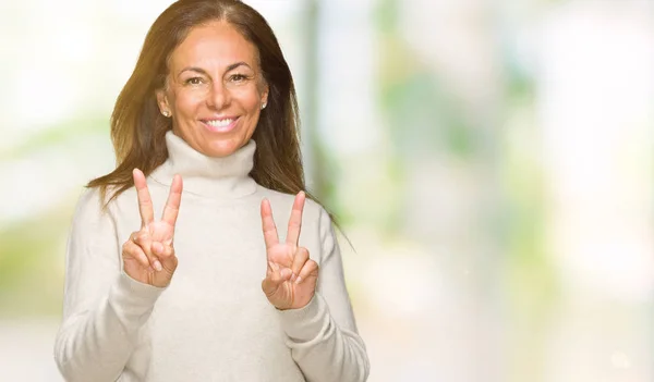 美しい中年成人女性の勝利のサインをやって指を表示するカメラを笑みを浮かべて隔離された背景に冬のセーターを着ています — ストック写真