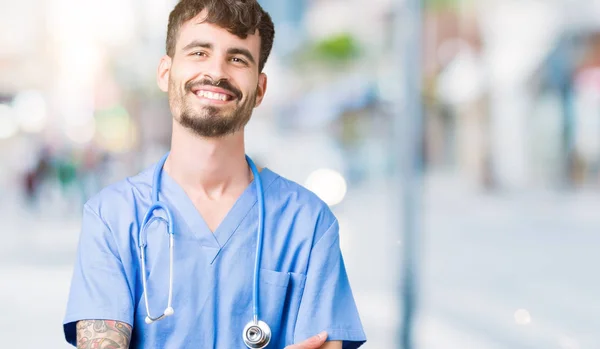 Young handsome nurse man wearing surgeon uniform over isolated background happy face smiling with crossed arms looking at the camera. Positive person.