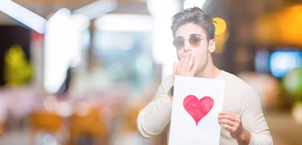 Jovem Bonito Homem Segurando Cartão Com Coração Vermelho Sobre Fundo — Fotografia de Stock
