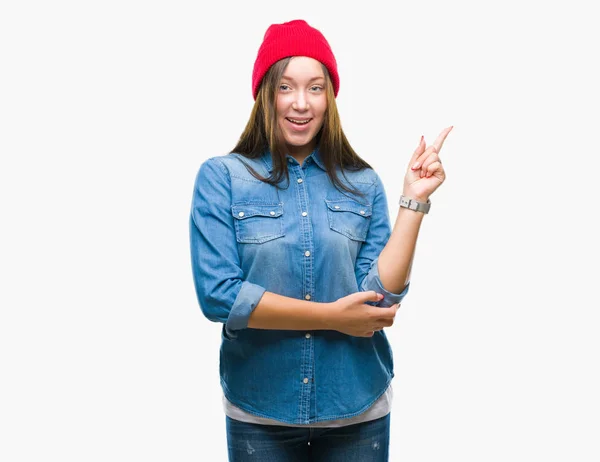 年轻的白种人美丽的妇女戴着羊毛帽在孤立的背景与一个大微笑在脸上 指着手和手指在一边看着相机 — 图库照片