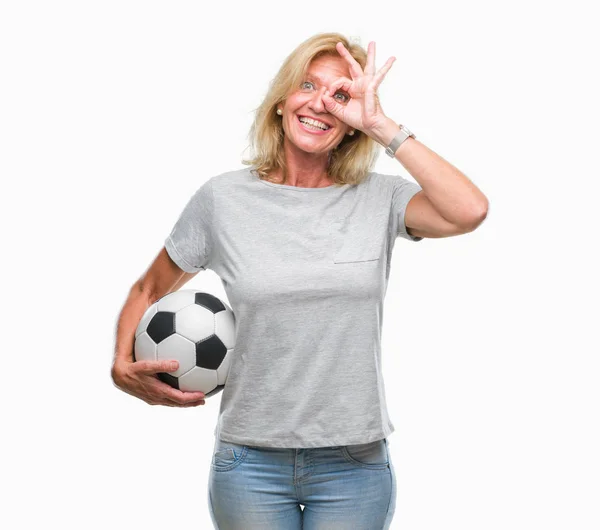 中年金发碧眼的女人拿着足球在孤立的背景与快乐的脸微笑做确定的标志用眼睛看着通过手指 — 图库照片