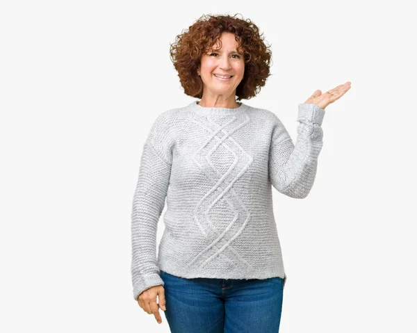 陽気な提示とカメラを見て手の手のひらで指している笑みを浮かべて分離の背景に冬のセーターを着て美しい中間エイガー年配の女性 — ストック写真