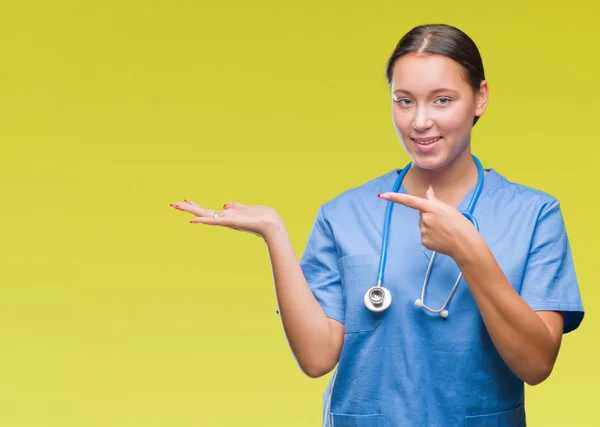 年轻的高加索医生妇女穿着医疗制服在孤立的背景惊讶和微笑的镜头 而提出用手和手指指指点点 — 图库照片