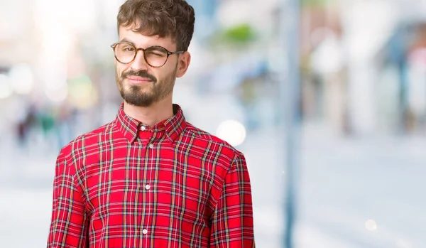 Young handsome man wearing glasses over isolated background winking looking at the camera with sexy expression, cheerful and happy face.