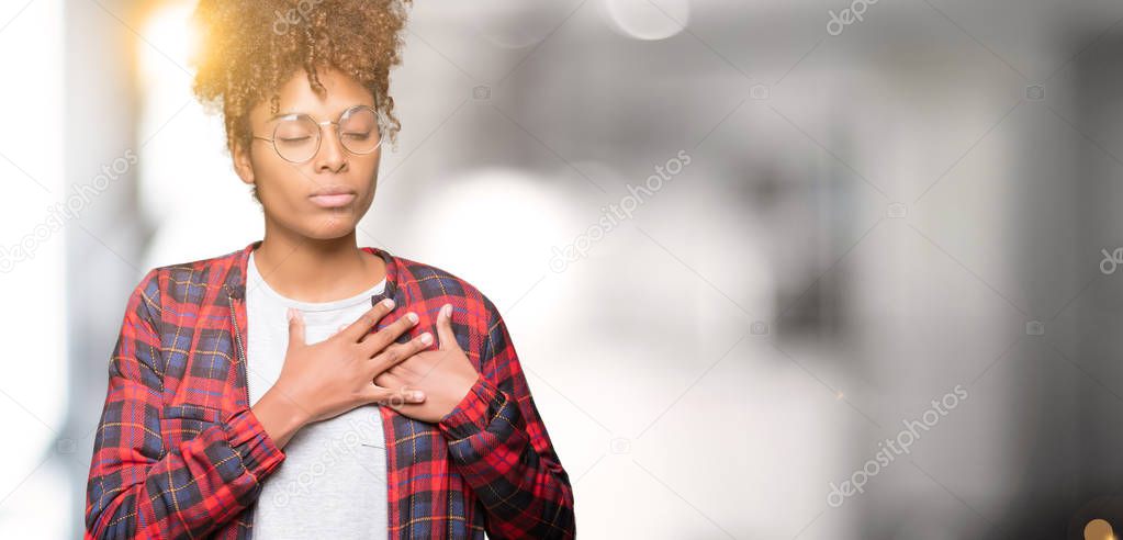 Beautiful young african american woman wearing glasses over isolated background smiling with hands on chest with closed eyes and grateful gesture on face. Health concept.