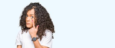 Kıvırcık saçlı beyaz t-shirt işaretleme göz izlerken seni jest, şüpheli ifade için giyen genç güzel kadın