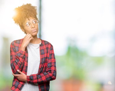 Güzel genç Afro-Amerikan kadın gözlük ile izole arka plan üzerinde çene düşünme hakkında soru, dalgın ifade ver. Düşünceli yüzüyle gülümsüyor. Şüphe kavramı.