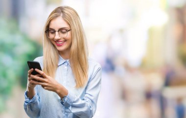 Genç güzel sarışın iş kadını ayakta ve diş gösterilen kendine güvenen bir gülümsemeyle gülümseyerek mutlu bir yüz ile izole arka plan üzerinde Smartphone kullanarak