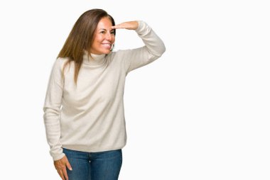 Üzerinde kış kazak giyen güzel orta yaş yetişkin kadın arka plan çok mutlu ve gülümseyen uzakta el ile üzerine kafa seyir izole. Arama kavramı.