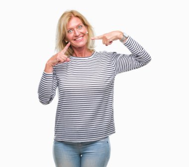 Orta yaş sarışın kadın kendinden emin gösterilen ve işaret parmakları diş ve ağız ile gülümseyen izole arka plan yüzünden. Sağlık kavramı.